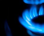 The image displays a close-up of a gas burner flame, characterised by vibrant blue flames that appear to flicker and dance. The flame is surrounded by a dark backdrop, highlighting the brightness and intensity of the gas flame, which is typically used in cooking or heating.