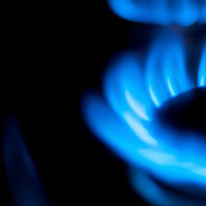 The image displays a close-up of a gas burner flame, characterised by vibrant blue flames that appear to flicker and dance. The flame is surrounded by a dark backdrop, highlighting the brightness and intensity of the gas flame, which is typically used in cooking or heating.